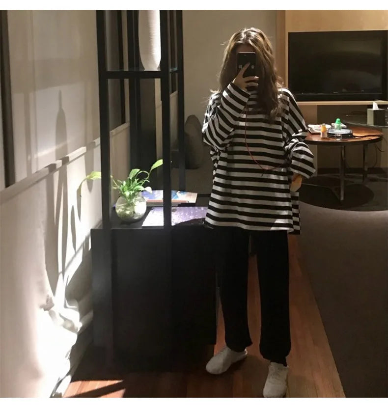 Girl taking a mirror selfie wearing a black and white striped shirt and dark pants in a living room.